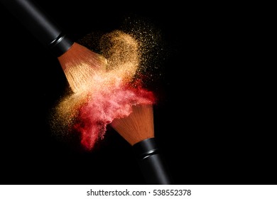 Makeup Concept. Stop Action View Of Two Makeup Brushes Applying Matching Red And Gold Powder Over Black Background With Copy Space For Text