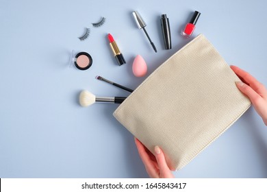 Make-up Cosmetic Bag In Female Hands On Blue Background. Stylish Makeup Artist Pouch With Beauty Products. Flat Lay, Top View