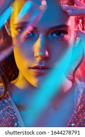 Make-up and cosmetics. Close up portrait of a gorgeous young woman with golden make-up posing with a champagne glass in a colored red, blue and yellow light. Party style. 