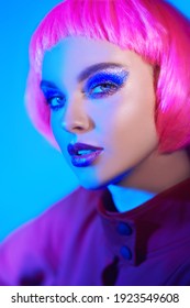 Makeup cosmetics and hairstyle. Portrait of a beautiful young woman with bright glitter makeup and pink hair posing in mixed color neon light. Beauty trends. 