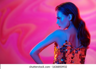 Make-up and cosmetics. Portrait of a beautiful young woman with golden make-up posing in a sparkling golden top in a colorful blue and pink light. Party style.