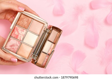 Makeup Eyeshadow Palette In Female Hands On A Pink Background With Feathers. Luxury Cosmetic Beauty Product.