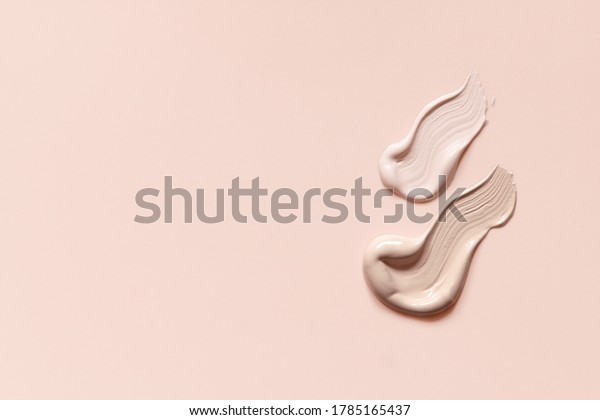 Makeup\
foundation cream strokes of different shades on skin tone color\
background. Nude pink creamy concealer\
smudges