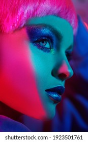 Make-up and hairstyle. Close-up portrait of a trendy fashion model girl with bright glitter make-up and pink hair posing in mixed color neon light. Beauty trends. 