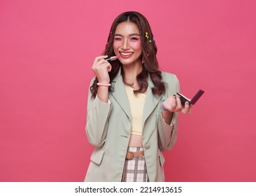 Makeup lipstick woman ready looking in pocket mirror. beautiful trendy young asian female fashion model putting makeup on pink background.
