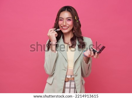 Makeup lipstick woman ready looking in pocket mirror. beautiful trendy young asian female fashion model putting makeup on pink background.