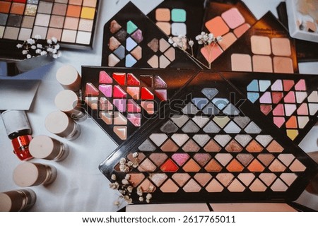 Makeup palettes featuring a range of vibrant eyeshadow colors, lipsticks, and blushes arranged artistically with small white flowers on a white background