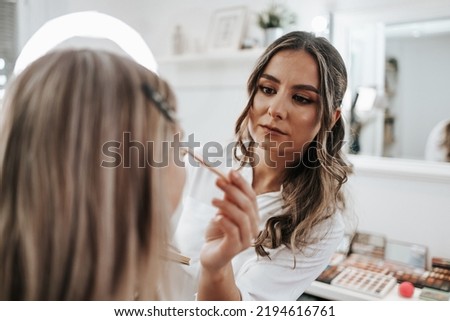 Makeup process. Professional artist applying make up on model face. Close up portrait of beautiful blonde woman in beauty saloon.
