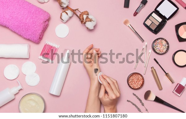 Make-up Remover Accessories. Flat lay\
background Womens hands try cosmetics, cotton branch, cotton pads,\
cosmetic bottle containers, pink towel, various make-up cosmetics,\
mascara, powder,\
lipstick.