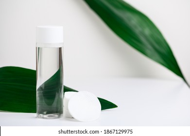 Makeup remover in plastic white bottle on a white background with green leaves, cotton cosmetic pads. Natural organic beauty liquid product. Micellar water for cleansing and moisturizing facial skin.