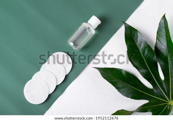 Make-up remover in\
small bottle and cotton discs on the green and white background.\
Cleansing skincare\
product