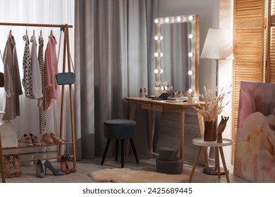 Makeup room. Stylish dressing table with mirror, chair and clothes rack indoors