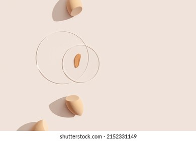 Makeup sponges for foundation cream, samples on glass disk on beige color background with shadows. Skincare beauty blender. Flat lay swatches from tone cream and sponge, minimal aesthetic trends