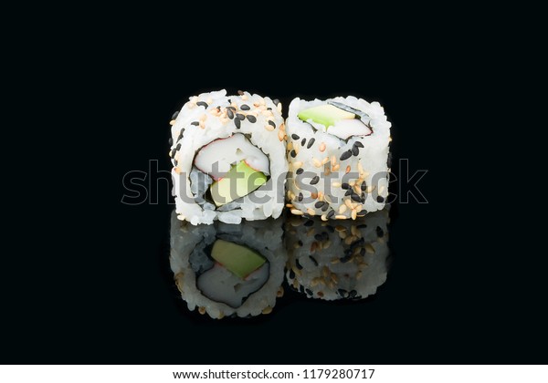 Maki California uramaki sushi isolated with surimi\
crab, avocado and sesame seeds on black background with reflection\
in front view