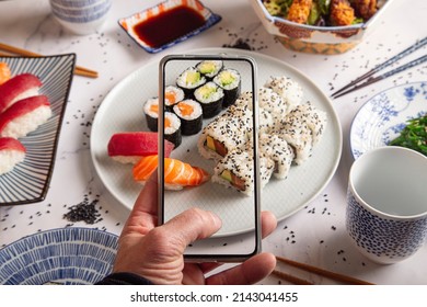 Maki rolls with smoked salmonMale hands make photography of sushi rolls with mobile phone. Top view.Young man taking a photo of a plate of sushi on a smartphone. Food photography with mobile phone.