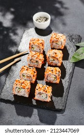 Maki sushi on dark slate. California maki with masago and sesame. Sushi roll with crab, cucumber inside, tobiko outside. Style concept japanese menu with black background, leaves and hard shadow