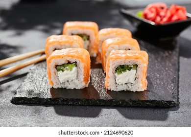 Maki sushi on dark stone table. Philadelphia maki with salmon. Sushi roll with cheese, cucumber inside, salmon outside. Style concept japanese menu with black background, leaves and hard shadow