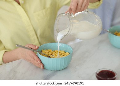 Making breakfast. Woman pouring milk from jug into bowl with cornflakes at white marble table, closeup - Powered by Shutterstock