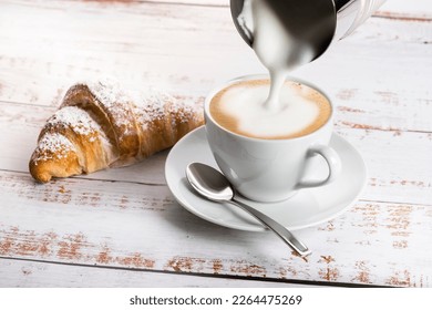 Making cappuccino with milk frother on wooden table with croissant. - Powered by Shutterstock