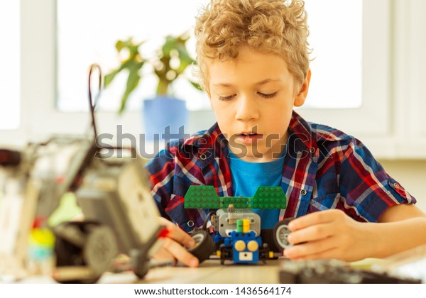 Making a car model. Nice blonde boy\
holding toy wheels in his hands while making a car\
model