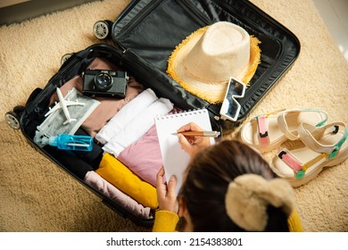Hacer una lista de las cosas a empacar para viajar. Mujer escribiendo papel toma nota y empaca maleta para las vacaciones escribiendo una lista de papel sentado en la habitación, preparar ropa en el equipaje, Viajar de vacaciones