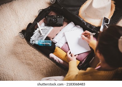 Making check list of things to pack for travel. Woman writing paper take note and packing suitcase to vacation writing paper list sitting on room, prepare clothes into luggage, Travel vacation travel