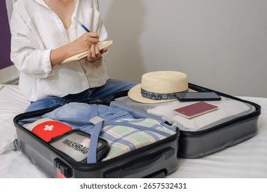 making a check list of things to pack for travel. woman writing checklist item on notebook and packing suitcase to vacation, prepare clothes, medicine, passport into luggage. travel vacation concept