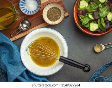 Making Dijon Vinaigrette In White Bowl, Overhead View With Whisk, Measuring Cup And Spoons, Salt, Pepper, And Green Salad