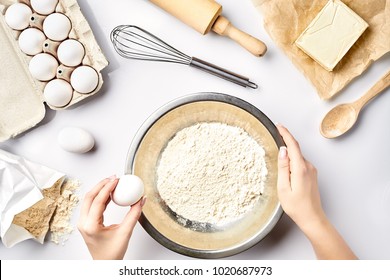 Making Dough Top View. Overhead Of Baker Hands Break Egg On Flour. Cooking Ingredients For Pastry On White Table.