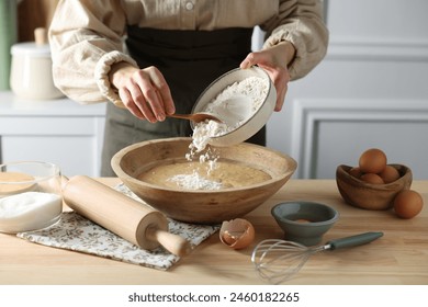 Making dough. Woman adding flour into bowl at wooden table in kitchen, closeup - Powered by Shutterstock