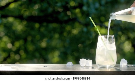 Making Drinks Outdoors. Pouring Carbonated Drink Into A Transparent Glass With Ice. Straw In A Drink. Many Ice Cubes In A Glass And Around. 