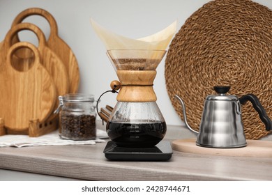 Making drip coffee. Glass chemex coffeemaker with paper filter, jar of beans and kettle on wooden countertop in kitchen - Powered by Shutterstock