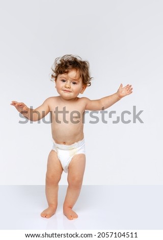 Making first steps. Portrait of happy toddler boy, baby in diaper walking isolated over white studio background. Concept of childhood, motherhood, life, birth. Copy space for ad