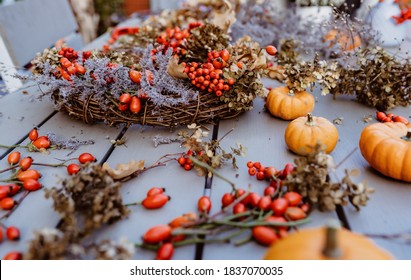 Making floral autumn door wreath from natural materials: colorful rosehip berries, rowan, dry flowers and pumpkins. Fall flower decoration workshop. Florist workplace. 