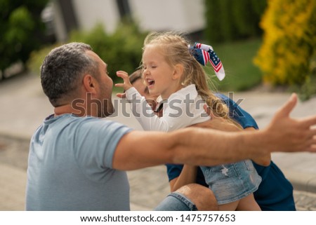 Making funny face. Cute blonde girl making funny face while hugging parents standing outside