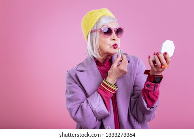 Making funny face. Cute lovely retired woman wearing pink dress making funny face coloring lips