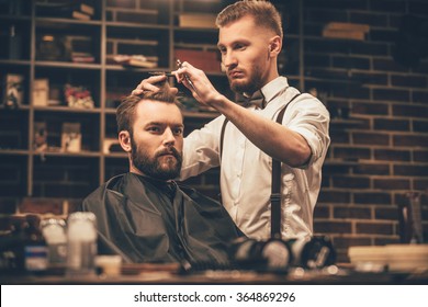 Making haircut look perfect. Young bearded man getting haircut by hairdresser while sitting in chair at barbershop - Powered by Shutterstock