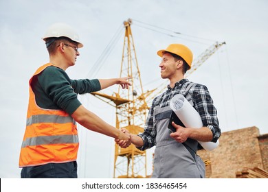 Making Handshake. Two Construction Workers In Uniform And Safety Equipment Have Job On Building Together.