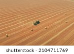 Making Hay Bales with Hay Baler using Farm Machinery. Tractor with Hay Baler compress a cut and raked hay and wheat straw into compact cylindrical bales on yellow dry field: aerial drone view shot.
