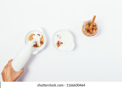 Making Healthy Breakfast Process, Top View. Women's Hand Pouring Milk Or Yogurt Into Bowl With Homemade Granola.