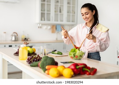 Making Healthy Meal. Portrait Of Cheerful Millennial Woman Cooking Fresh Vegetarian Food Standing In Kitchen, Slim Fit Lady Mixing Salad In Glass Bowl Using Wooden Spoons, Free Copy Space