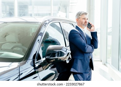 Making his choice. Serious mature grey hair beard businessman salesman wearing blue formal suit standing next to new car in showroom using his smartphone. - Powered by Shutterstock