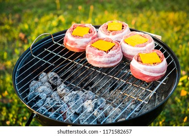 Making Home Made Beer Can Bacon Burgers On Barbecue Grill. Preparing Stuffed Patties, Wrapped  In Bacon And Grilling On Indirect Heat In Nature At Back Yard BBQ Picnic. Low And Slow Technique With Sun