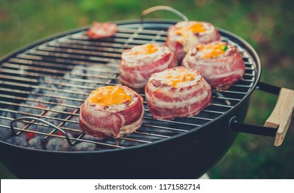 Making Home Made Beer Can Bacon Burgers On Barbecue Grill. Preparing Stuffed Patties, Wrapped  In Bacon And Grilling On Indirect Heat In Nature At Back Yard BBQ Picnic. Low And Slow Technique With Sun