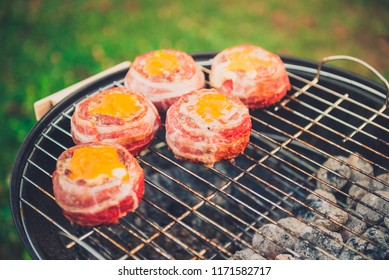 Making Home Made Beer Can Bacon Burgers On Barbecue Grill. Preparing Stuffed Patties, Wrapped  In Bacon And Grilling On Indirect Heat In Nature At Back Yard BBQ Picnic. Low And Slow Technique With Sun