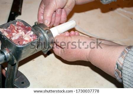 Making homemade sausage at home. Stuffing pork intestine with meat.The picture shows a woman pulling gut on the tube of a meat grinder. You can see part of the hands, the meat grinder, the meat in it