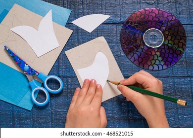 Making homemade toy fish from the CD. Paper, CD, scissors, patterns on a blue wooden table. Handmade children's project. Step by step photo instructions. Step 2: The child draws the details toys