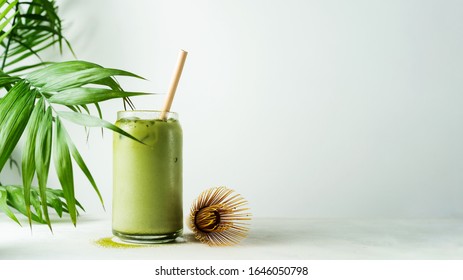 Making Japanese iced matcha latte, green tea with milk, soy milk, traditional matcha tools, with bamboo straw in glass on white background.