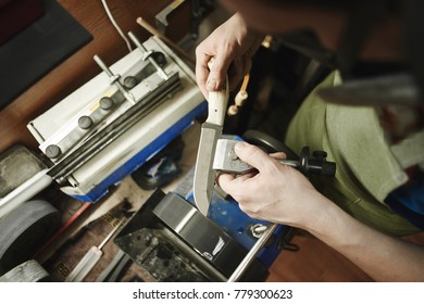 Making of a knife. Master sharpens a blade on the machine closeup in the Studio
