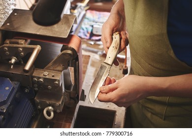 Making of a knife. Master sharpens a blade on the machine closeup in the Studio